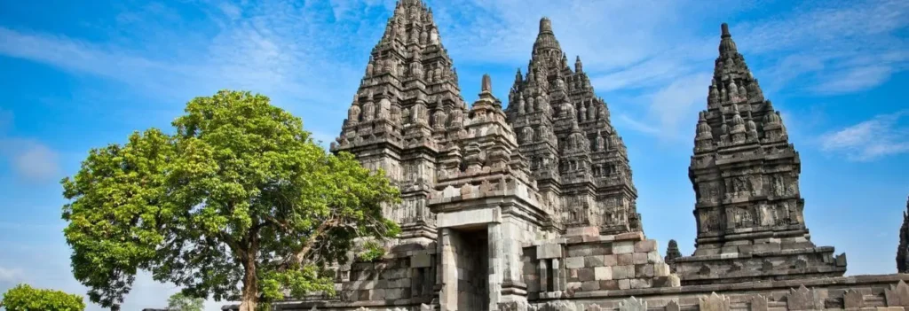 The tall stone spires of Prambanan Temple complex under a blue sky